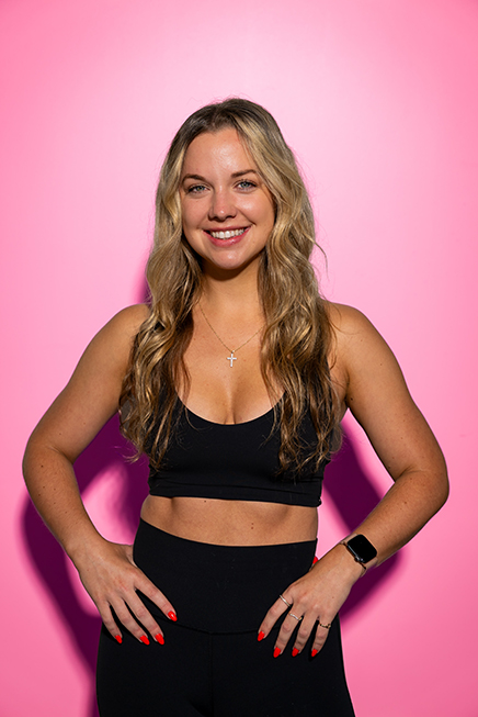Smiling Sweat House OC instructor against a pink backdrop