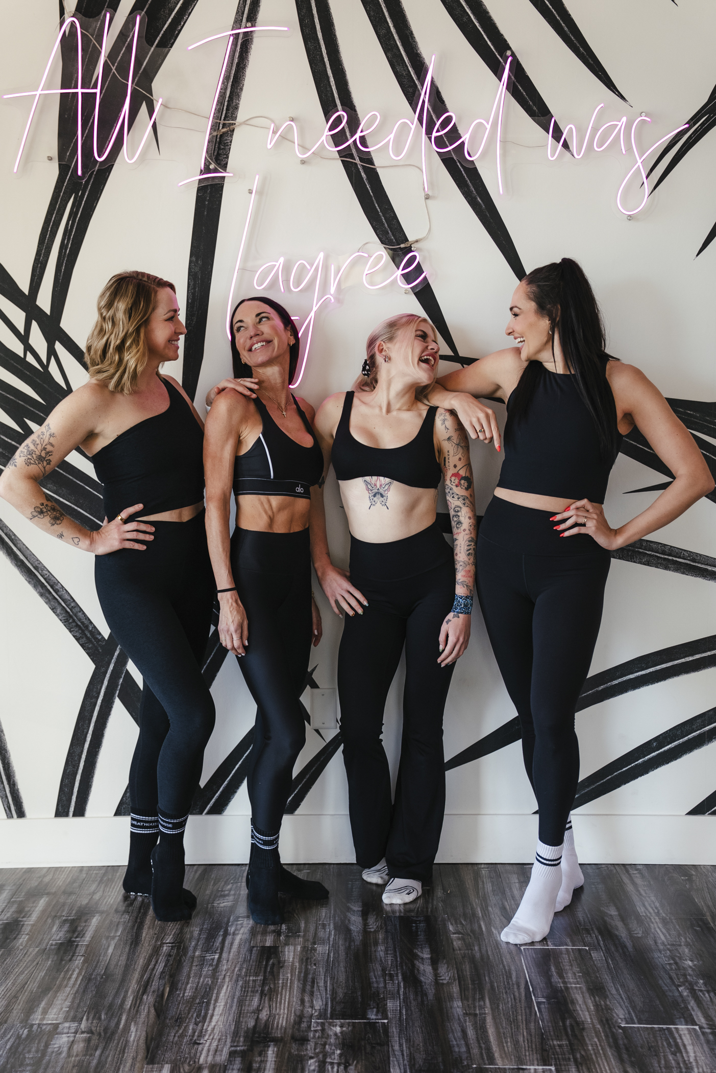 Four instructors laughing together beside the neon Lagree sign